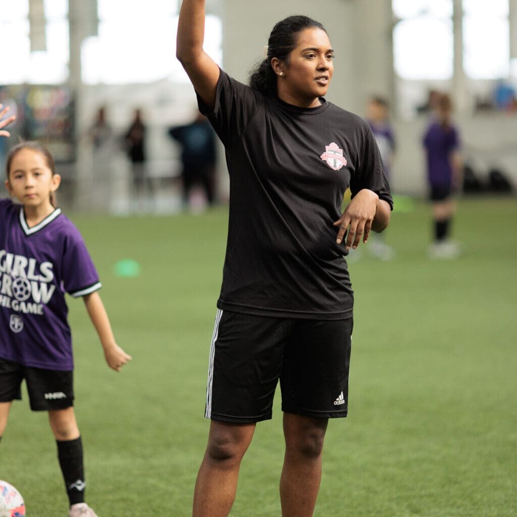 Soccer coach wearing black t-shirt and black shorts holds one hand up on the air.